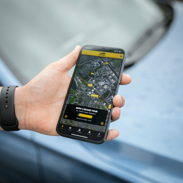 Eine Hand hält ein Smartphone mit einer Kartenanwendung, im Hintergrund ein blauer Pkw.